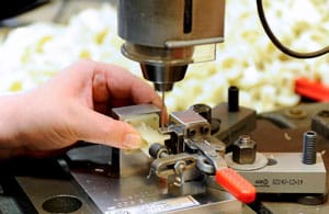 Jemand arbeitet mit einer Standbohrmaschine an einem Werkstück.