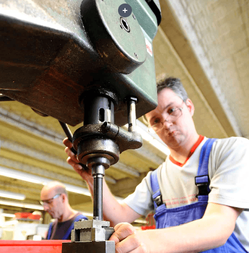 Foto eines Mannes, der in der Werkstatt mit einer Tischbohrmaschine arbeitet.